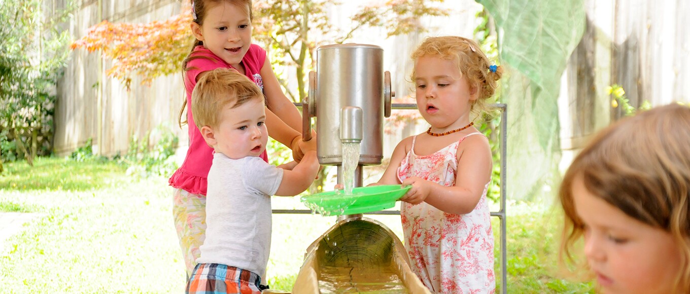 Eine Gruppe Kinder spielt draußen an der Wasserpumpe