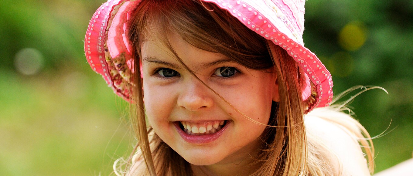 Ein Mädchen in einem pinken Hut lächelt in die Kamera